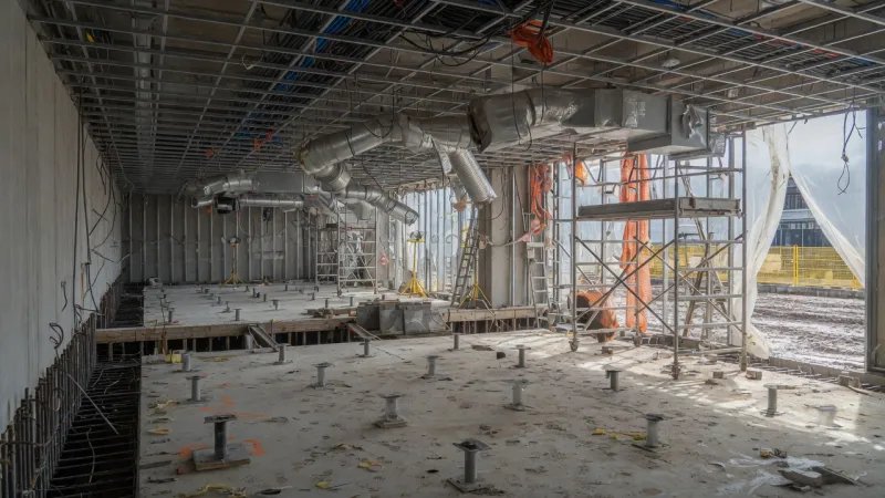 Unfinished stick-built data hall with raised-floor pedestals, ductwork, and scaffolding